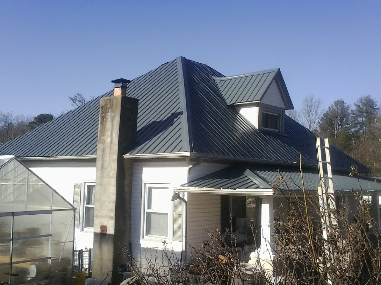 Dark blue standing seam metal roof on a white farmhouse with dormer — Slate & Tile Roof Repair by Roofing Brothers in Fawn Grove