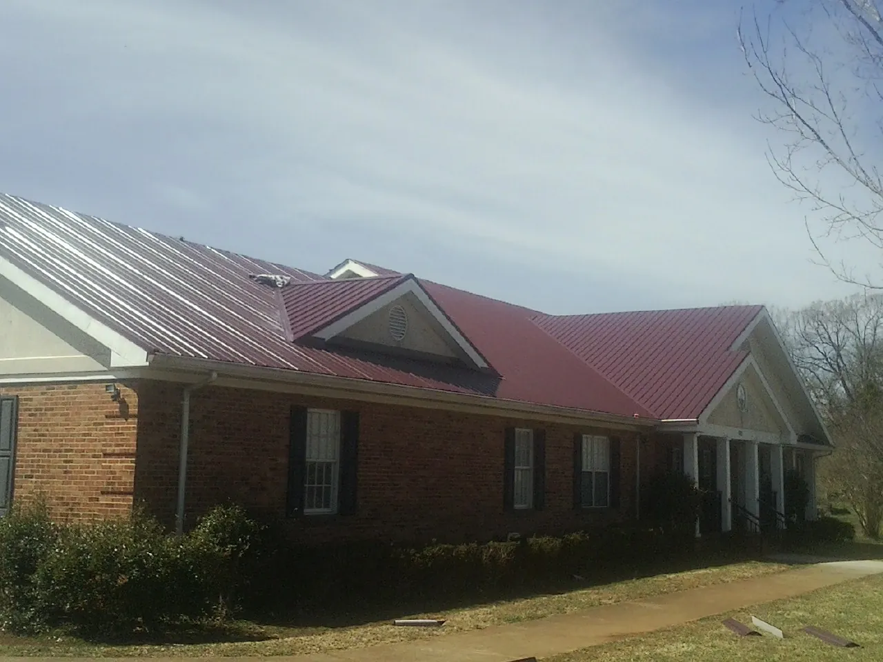 Red metal roof with gabled entries on a long brick building, from a Hail Damage Roof Repair job in Fawn Grove