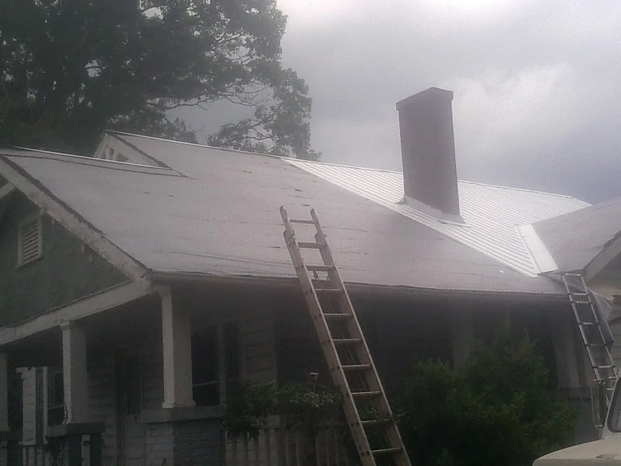 Ladders against a metal roof on an older home with a brick chimney in Fawn Grove