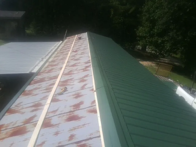 Old rusted panels beside newly installed green metal roofing — Wind Damage Roof Repair by Roofing Brothers in Fawn Grove