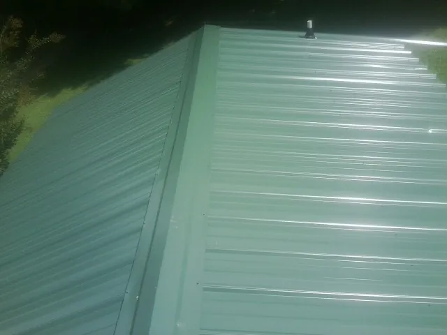 New green metal panels meeting at the ridge of a roof — Flat Roof Repair work by our crew in Fawn Grove
