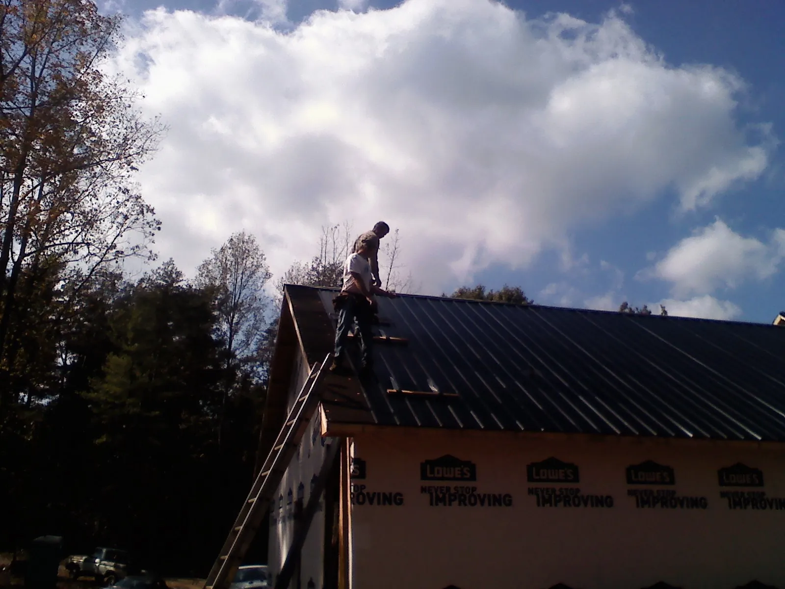 Roofer fastening dark metal panels high against a cloudy sky, from a Roof Inspection job in Fawn Grove