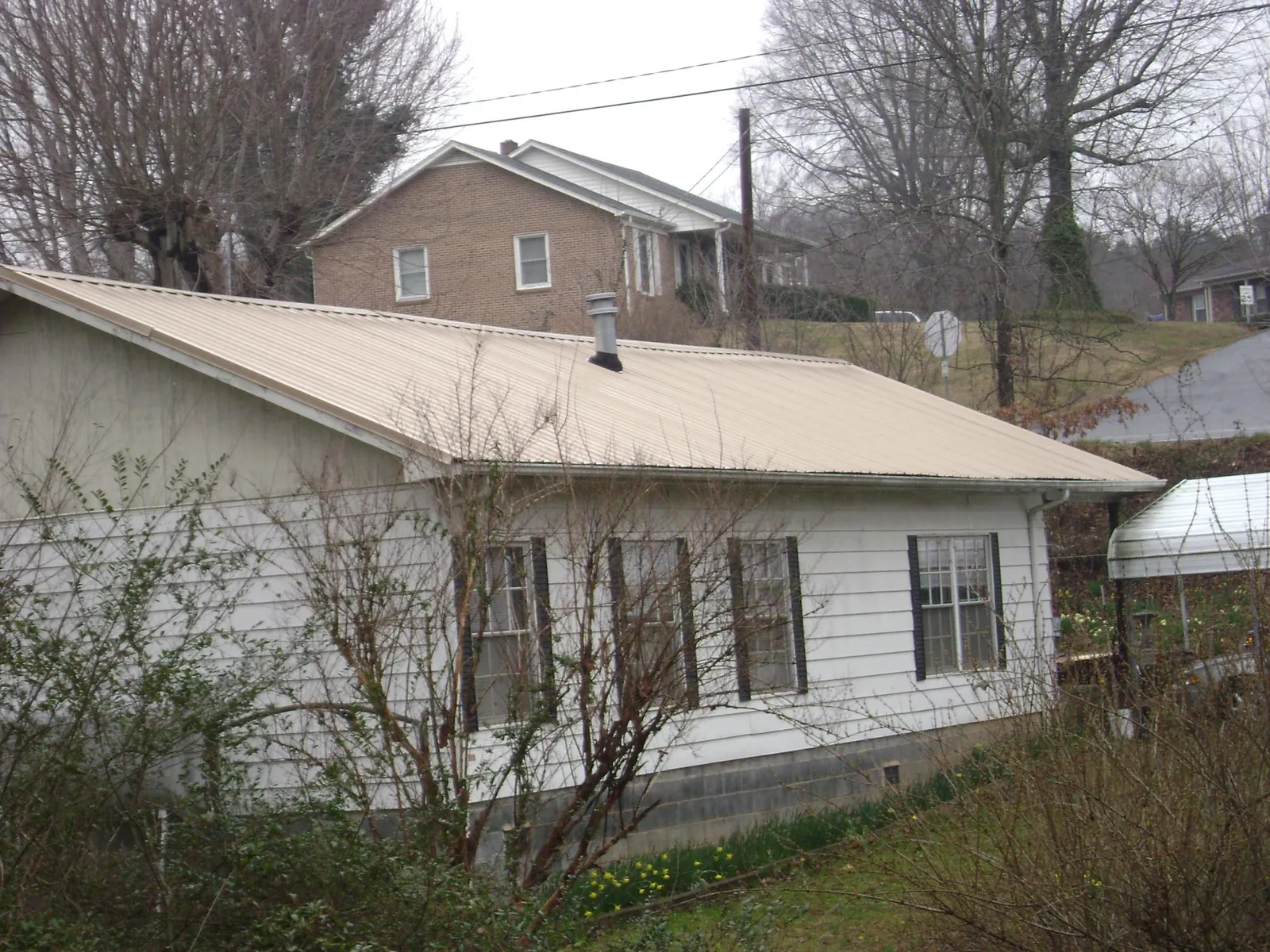 Tan metal roof on a white sided house set into a hillside — Commercial Roofing by Roofing Brothers in Fawn Grove